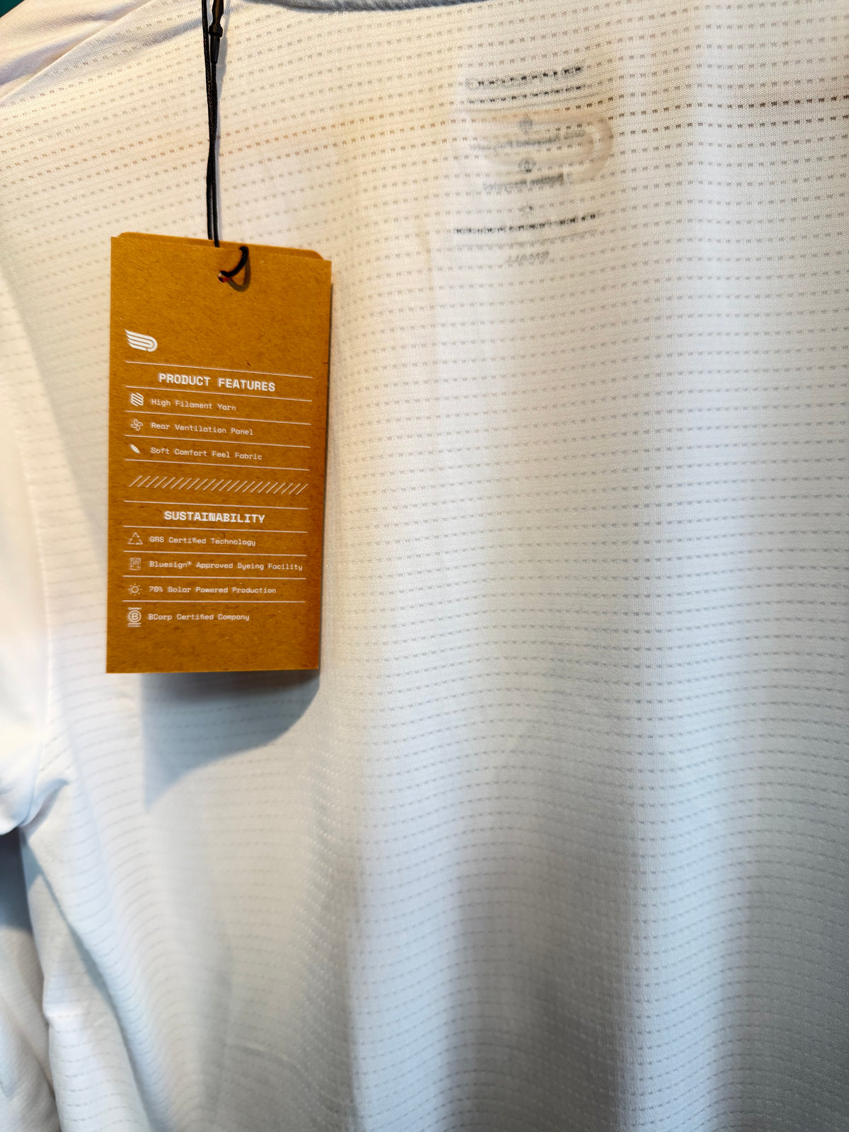 Close-up of a white textured athletic shirt with a brown product information hangtag attached near the collar.